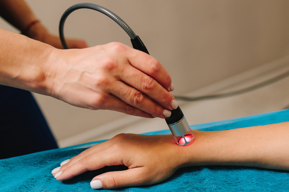 A laser is used on a woman's arm. The laser glows with red light.